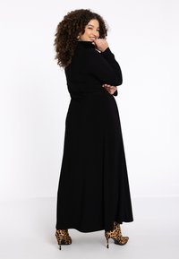 Robe noire à manches longues avec un corsage ajusté et une jupe fluide, associée à des chaussures à talons hauts en imprimé léopard. Tissu lisse avec un design épuré.