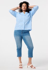 Chemise brodée bleu clair avec fermeture à boutons, associée à un jean cropped bleu avec des ourlets cloutés et des sandales à talons beiges.