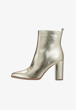 Metalen gouden enkellaars met een spitse neus, gladde textuur en een stevige hoge hak. Voorzien van een trekhaak aan de achterkant voor gemakkelijke aan- en uittrekken.