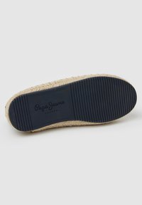 Suela de alpargata con una textura tejida beige, que presenta una base de goma negra con surcos horizontales y el nombre de la marca en relieve.