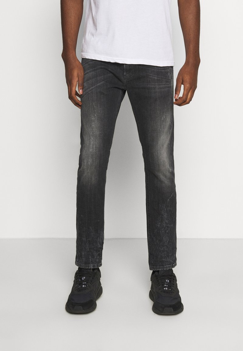 Tmavě šedé džíny s vybledlým povrchem, rovný střih a jemné efektové skvrny. V kombinaci s černými teniskami a bílým tričkem.