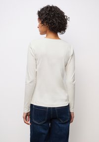 Top a maniche lunghe in maglia di colore bianco sporco, con scollatura quadrata sul retro, abbinato a jeans blu scuro, che mette in mostra uno stile casual.