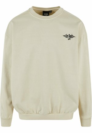 Sweatshirt beige en tissu doux, avec un col rond, des manches longues, des poignets côtelés, et un logo noir brodé sur la poitrine.