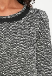 Țesătură de tricot în zig-zag alb-negru, cu o textură netedă. Prezintă un guler rotund negru și un design cu mâneci bufante.