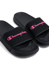 Chanclas negras con correas perforadas en negro y logo rosa de "Champion". Plantilla texturizada negra para agarre y comodidad.