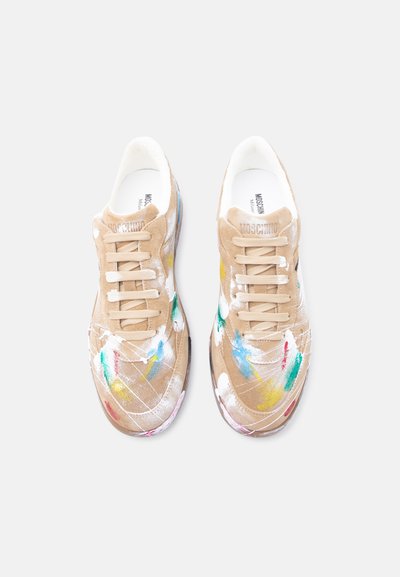 Par de zapatillas deportivas de ante beige con salpicaduras de pintura multicolor y cordones beige, vistas desde arriba sobre un fondo blanco.
