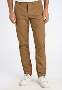 Khakifärgade chinos i lätt tyg, med rak passform, framfickor och knäppning, kombinerat med vita sneakers.