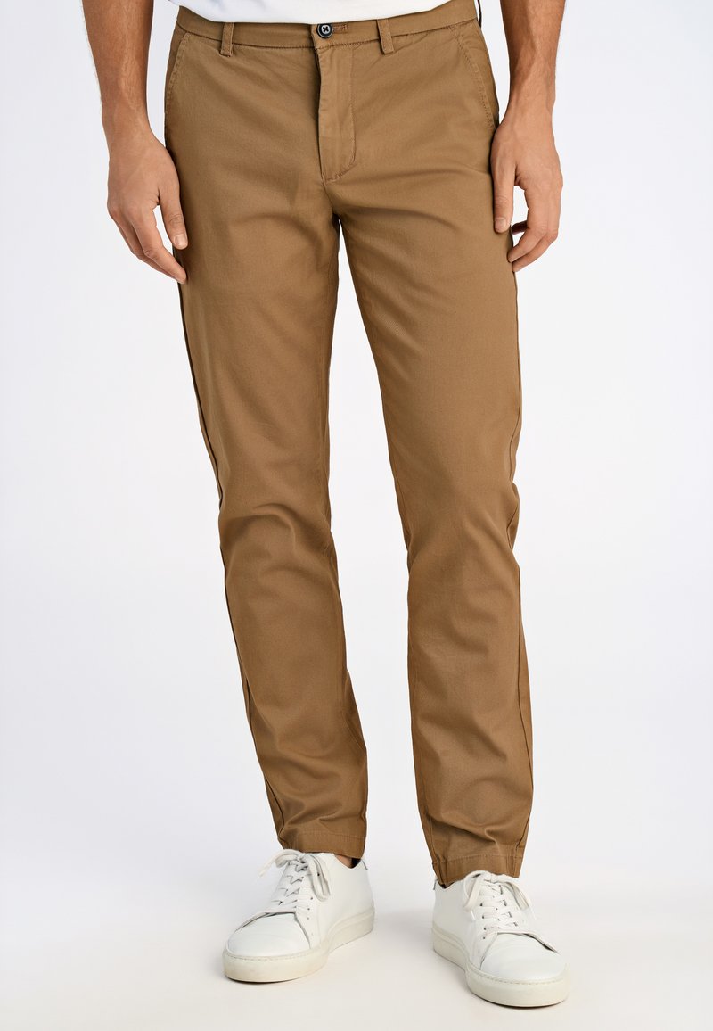 Khakifärgade chinos i lätt tyg, med rak passform, framfickor och knäppning, kombinerat med vita sneakers.