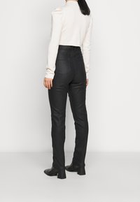 Pantalones negros de cintura alta, hechos de un material suave, con una forma ajustada, detalles de costura y perneras estrechas, combinados con un suéter ligero.