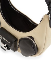 Beige canvas shoulder bag with black leather accents, zippered compartments, and a smooth texture. Features a bold brand logo.