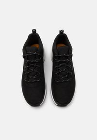Černé sportovní boty vyrobené z nubuku a síťoviny, s texturovanými tkaničkami, polstrovanou podrážkou a žlutou stélkou. Bílá podrážka s logem.