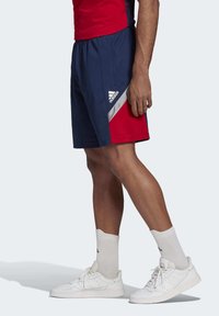 Niebieskie i czerwone spodenki sportowe z elastyczną talią, z przekątnym wzorem kolorowych bloków i białym logo "adidas".