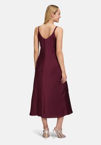 Burgunderfarbendes Satin-Midikleid mit schmalen verstellbaren Trägern, einem V-Ausschnitt hinten und einer fließenden Silhouette. Kombiniert mit hochhackigen Sandalen mit Riemchen.