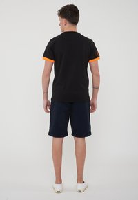 T-shirt nera con maniche corte arancioni, abbinata a pantaloni corti blu navy. La t-shirt presenta un piccolo logo sulla spalla. Tessuto morbido, vestibilità casual.
