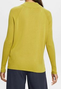 Pull côtelé à manches longues de couleur jaune vif. Il présente un col montant et une coupe décontractée, avec une texture lisse et des détails de couture subtils.