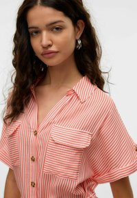 Rot-weiße gestreifte Bluse mit Kragen, kurzen Ärmeln und zwei Brusttaschen, Vorderseite mit Knopfverschluss und weichem Stoff.