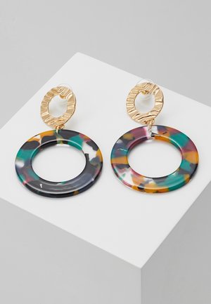 Gouden metalen oorbellen in oorringvorm met structuur, met grote kleurrijke open harscirkels in tinten teal, oranje, zwart en paars, gepresenteerd op een wit blok.