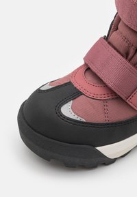 Rubber-soled winter boot with pink textile upper, black synthetic toe cap, and Velcro strap. Features silver accents and textured surface.