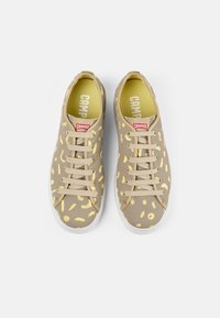 Beige sneakers med gula abstrakta mönster, platta snörningar, gummisulor och en röd Camper-logotyp på tungan. Strukturerad kanvas ovandel.