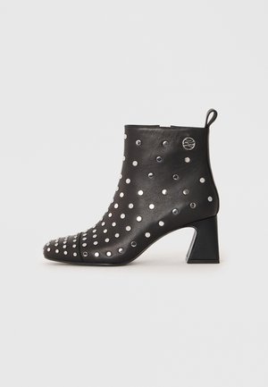 Black leather ankle boot with silver metal stud accents, pointed toe, and a chunky heel. Features a pull tab on the back for easy wear.