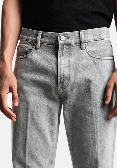 Jeans in denim grigio chiaro con taglio dritto, dotati di chiusura a bottone e cinque tasche. Texture liscia e design minimalista.