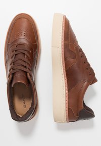 Brune lædersneakers med perforeret tå, brune snørebånd og cremet gummisål. Har kontrasterende brune detaljer på hælen.