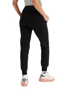 Czarne dresy o luźnym kroju, z elastycznym paskiem w talii i mankietami przy kostkach, zestawione z masywnymi białymi sneakersami z różową podeszwą.