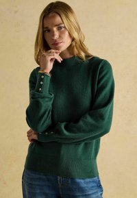 Roheline kudumipealistik ribidega kaelusest ja nööpide aktsendiga varrukatel. Pehme tekstuur ja lõdva istuvusega, sobib kokku siniste teksadega.