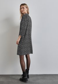 Schwarz-weißer gemusterter Kleid mit lockerer Passform, Dreiviertelärmeln und Rundhalsausschnitt, kombiniert mit schwarzen Knöchelstiefeln und transparenten Strumpfhosen.