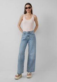 Lichtroze getailleerde tanktop, hoogwaardige lichtblauwe wijde jeans, beige platform sandalen en donkere zonnebril tegen een neutrale achtergrond.