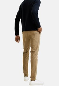 Pantaloni khaki in cotone, design slim-fit, vita con tasche, abbinati a sneaker bianche e un maglione blu navy.