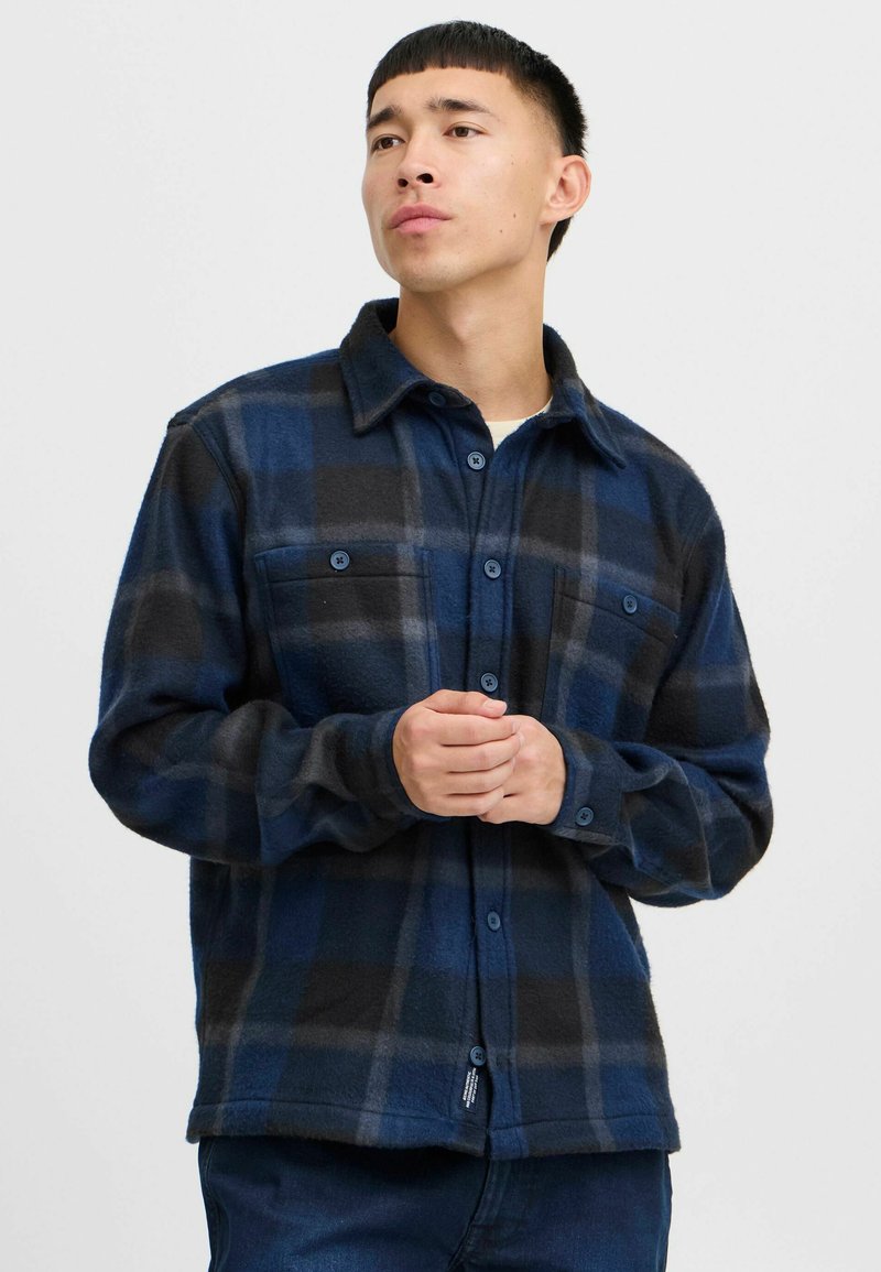 Marineblauwe en zwarte geruite flanellen shirt met twee borstzakken, knoopsluiting aan de voorkant en een zachte textuur. Lange mouwen met knoopmanchetten.