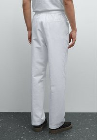 Witte katoenen broeken met een elastische tailleband, rechte snit en achterzakdetail. In combinatie met donkere schoenen op een gestructureerd oppervlak.