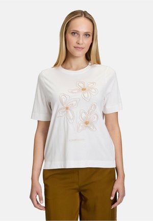 T-shirt blanc à manches courtes avec trois fleurs brodées en beige et or, avec le texte "JARDIN DE FLEURS" en dessous. Tissu en coton doux et léger.