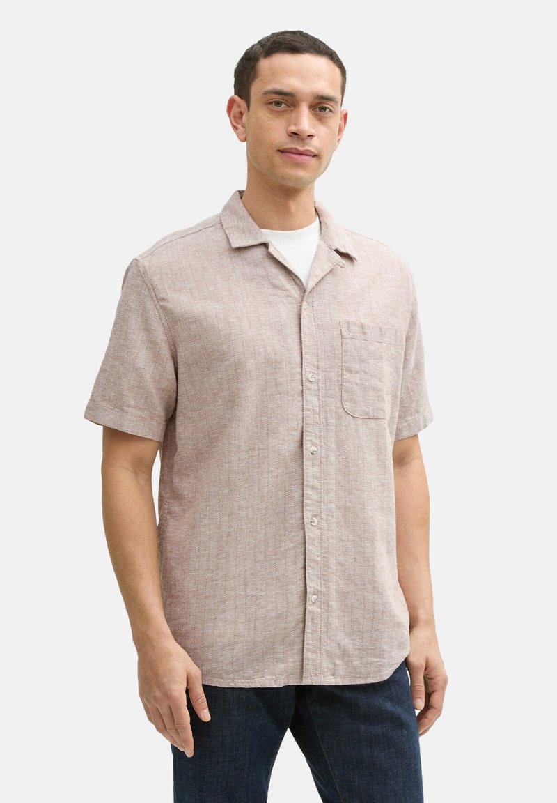 Kurzarm-Hemd mit Kragen in Hellbeige mit strukturiertem Gewebe, ausgestattet mit einer einzelnen Brusttasche und weißen Knöpfen, kombiniert mit dunklen Jeans.