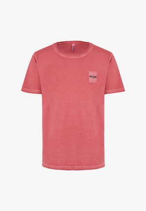 T-shirt rossa in cotone con maniche corte, colletto rotondo e un piccolo logo bianco "Moschino" su una tasca. Tessuto morbido con un leggero effetto di sbiadimento.
