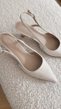 Zapatos de tacón slingback de charol blanco con punta afilada, un pequeño tacón bloque y acentos recortados en los laterales. Plantillas interiores suaves en color beige.