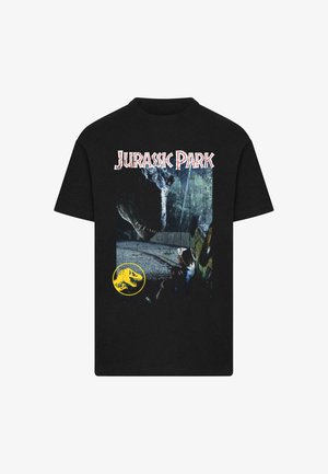 Must mustaline T-särk, millel on "Jurassic Park" tekst, dinosauruse pea, mis ulatub üle istuva mehe läheduses oleva sõiduki, ja allraakonnaga kollane dinosauruse logo.