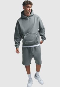 Grå hettegenser med en frontlomme og justerbar snor, parret med matchende shorts, båret med hvite joggesko og ankelsokker.