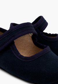 Chaussures en daim bleu marine avec une texture douce, dotées d'un bout rond et de sangles élastiques chevauchantes pour un ajustement sécurisé. Doublure intérieure en matériau naturel.