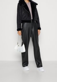 Svart jacka med fuskpälskrage, ljuslila topp, svarta fusk läderbyxor, vit handväska och vita sneakers. Enkel, modern design.