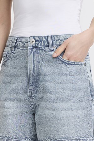 Personne portant un short en jean bleu clair avec une main dans la poche avant et un haut blanc rentré.