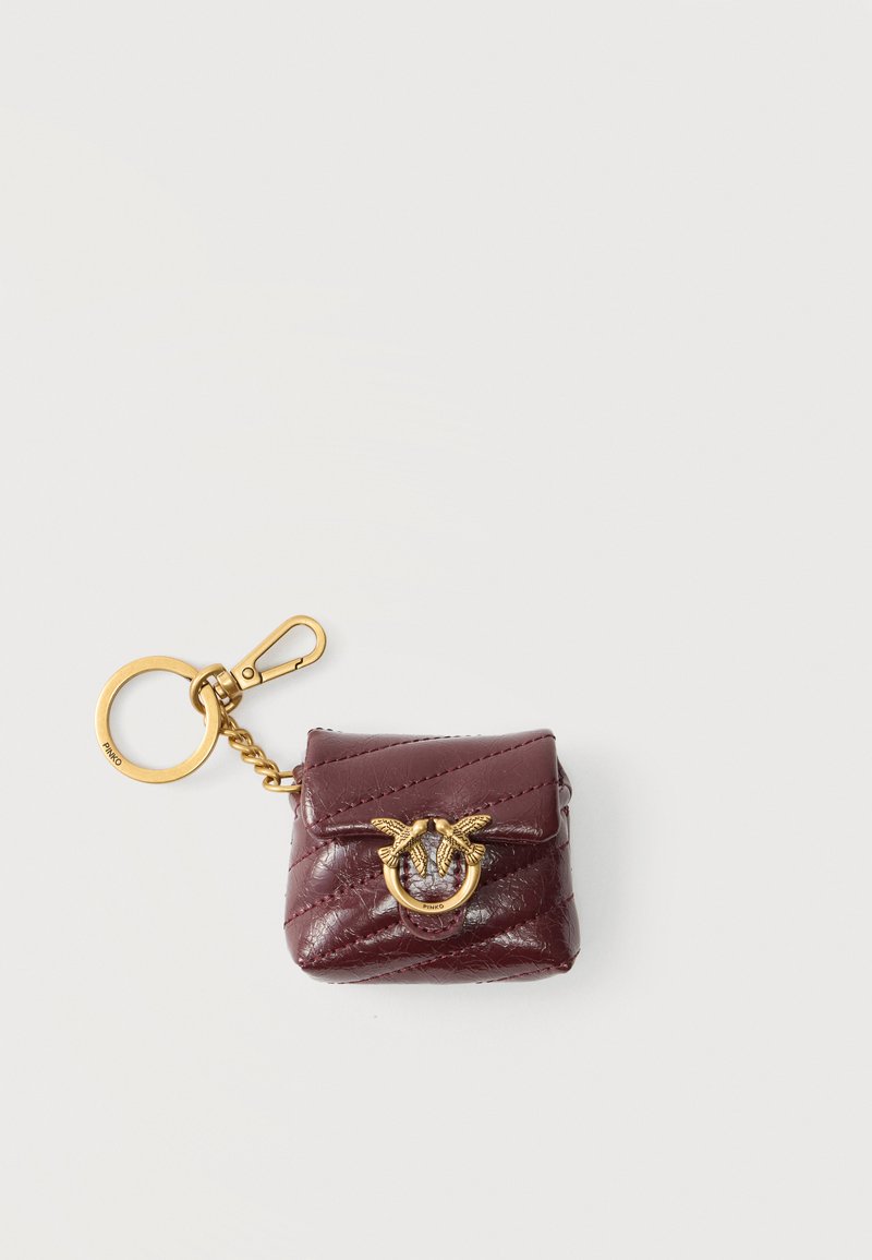 Μπορντό καπιτονέ δερμάτινη θήκη μπρελόκ με λεπτομέρεια χρυσού τόνος δαχτυλίδι με πουλιά και κρίκο μπρελόκ με κλιπ σε ανοιχτό φόντο.