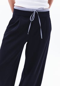 Pantaloni a gamba larga navy con cintura elasticizzata a righe, dotati di un laccio e pieghe frontali per un tocco di stile e comfort aggiuntivo.