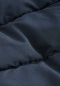 Fabric de chaqueta acolchada azul marino con una textura suave, que presenta secciones acolchadas y un sutil brillo, mostrando un acabado de costura fina a lo largo de los bordes.