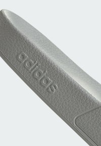 Šedé pantofle Adidas s texturovaným svrchním dílem a logem, plochou podrážkou a minimalistickým designem. Materiál vypadá jako syntetika.