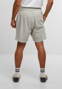 Shorts grii deschis din bumbac, cu un talie elastică, buzunare laterale și un buzunar pe spate. Purtați cu șosete cu dungi și pantofi casual.