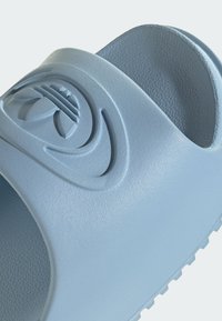 Sandale bleu à enfiler avec semelle texturée et logo vague en relief sur la bride, fabriquée en matériau lisse de type caoutchouc.