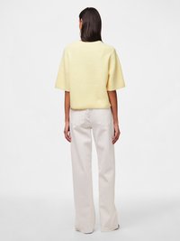 Yellow short-sleeve sweater with a loose fit, ribbed texture, and round neckline, paired with off-white wide-leg pants.