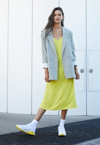 Blazer à carreaux surdimensionné en bleu et blanc, superposé sur une robe de nuit jaune vif. Assorti à des baskets blanches avec des accents jaunes.